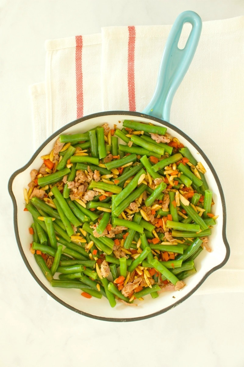 overhead shot of green beans with prosciutto in a fry pan with a blue handle, set on a yellow napkin with red stripes