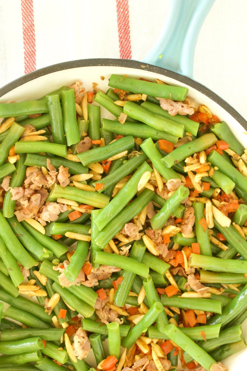 overhead shot of green beans with prosciutto in a fry pan with a blue handle, set on a yellow napkin with red stripes