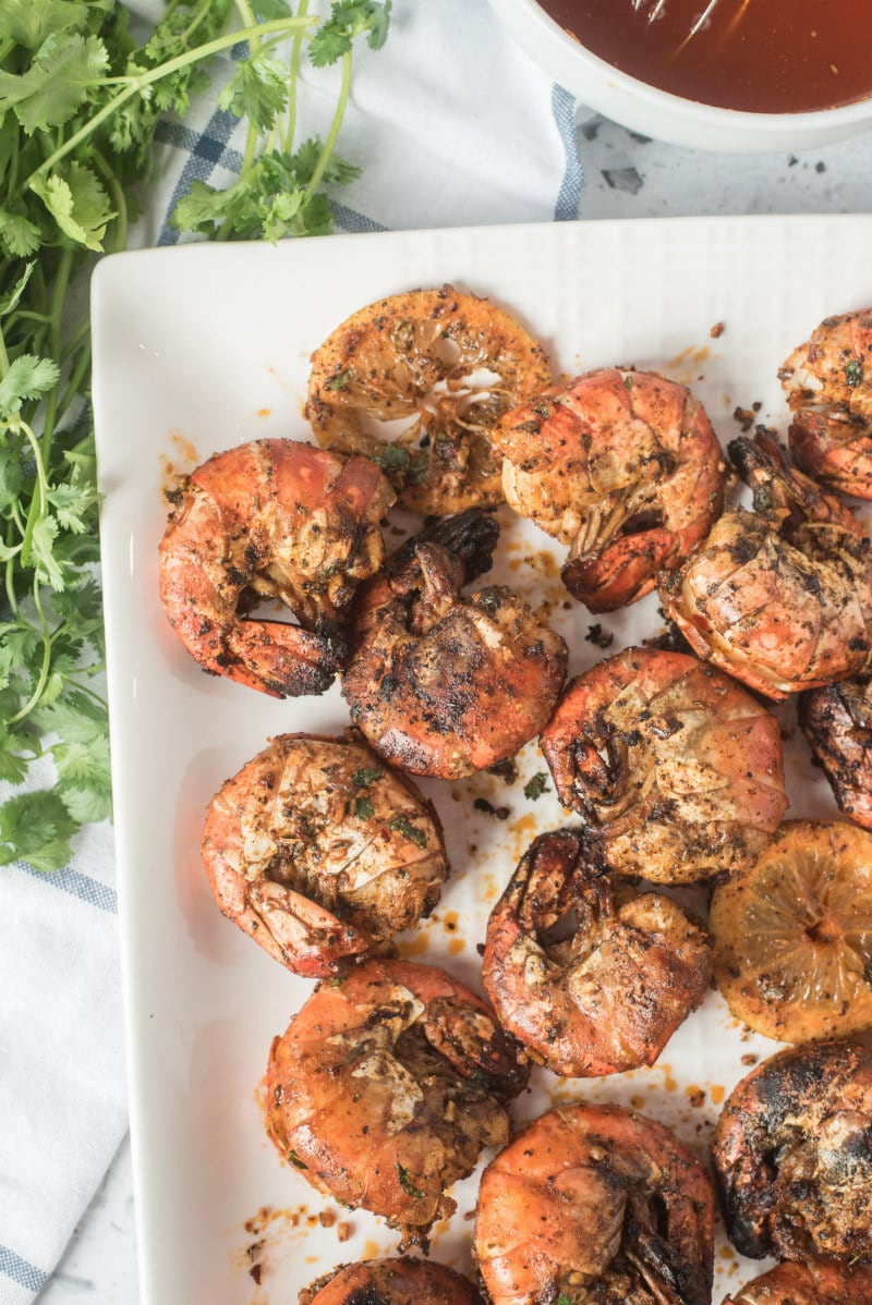 grilled jumbo shrimp on a white platter with white and blue plaid napkin underneath. peek of fresh cilantro and lemon cilantro butter on the side