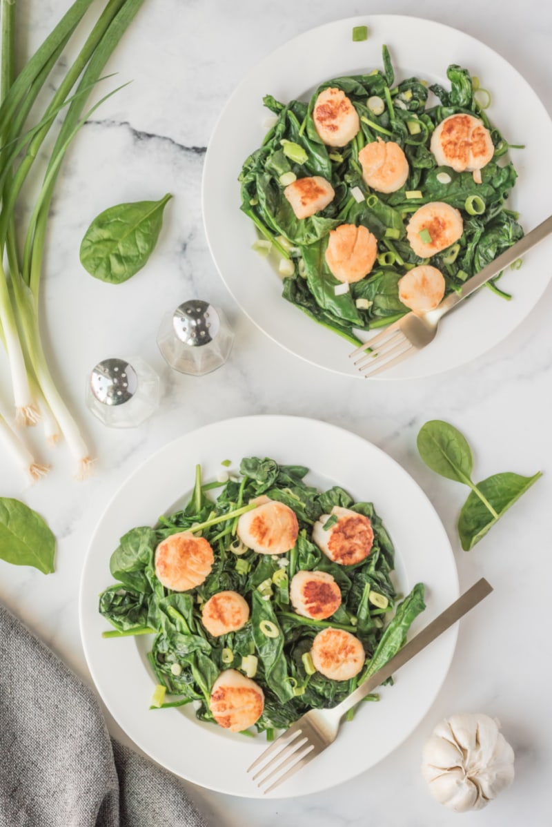 two plates of spinach topped with seared jumbo scallops