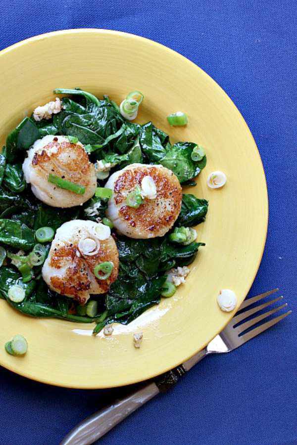 Seared Jumbo Scallops on a bed of spinach on a yellow plate