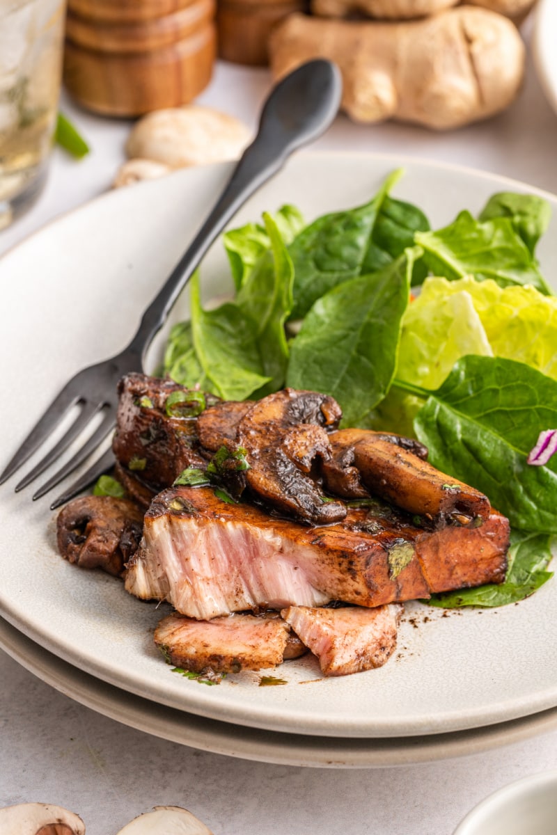 fork cutting into tuna steak on plate with salad