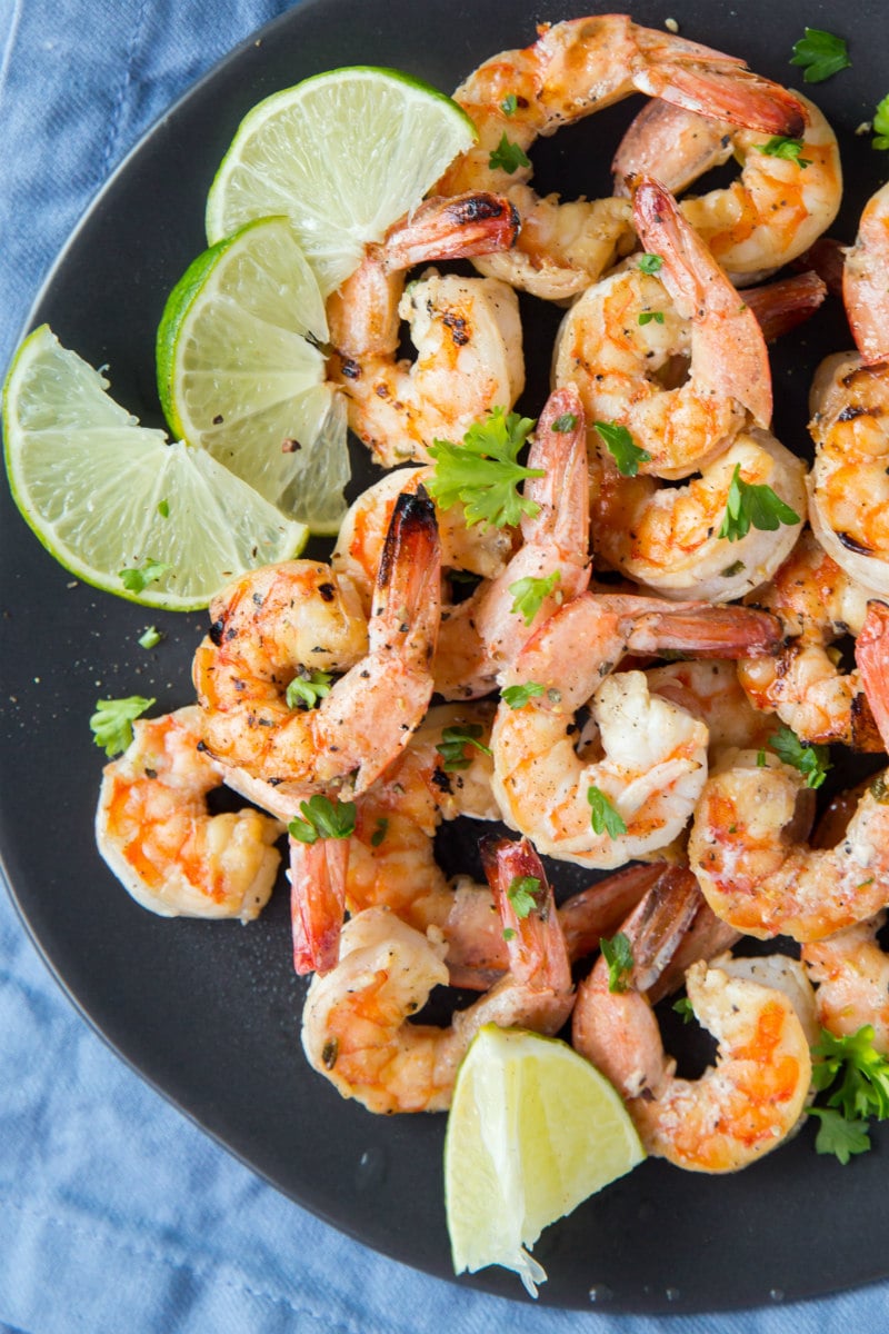 Marinated Grilled Shrimp on a black plate with lime garnish and a blue napkin underneath