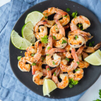 Marinated Grilled Shrimp on a black plate set on a blue napkin with lime and cilantro garnish