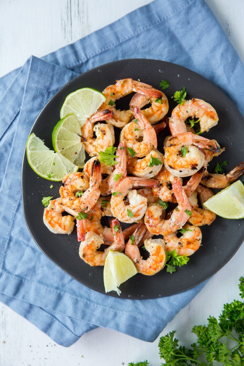 Marinated Grilled Shrimp on a black plate set on a blue napkin with lime and cilantro garnish