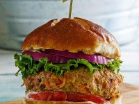 turkey garden burger dressed with lettuce and tomato in a bun with a sandwich pick on top, sitting on a wooden cutting board. galvanized metal tub in background