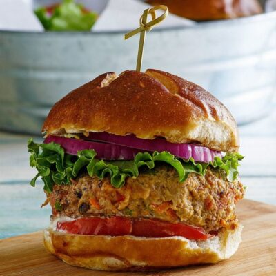 turkey garden burger dressed with lettuce and tomato in a bun with a sandwich pick on top, sitting on a wooden cutting board. galvanized metal tub in background