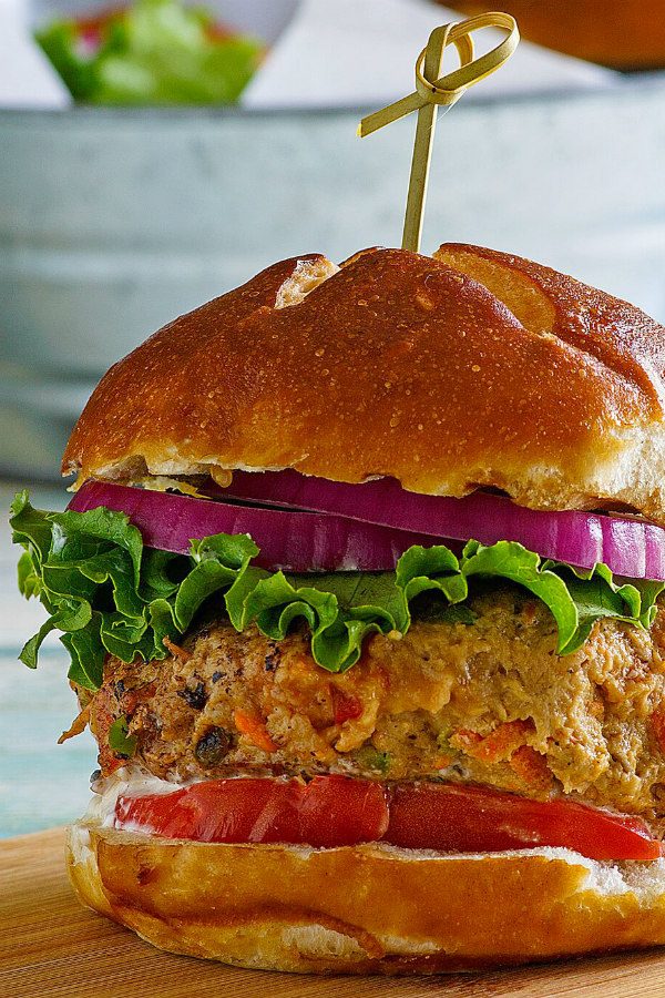 close up of Turkey Garden Burger dressed with red onion, lettuce and tomato on a bun with a sandwich pick