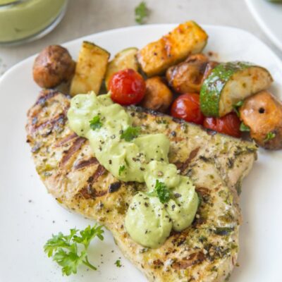 grilled swordfish topped with avocado mayonnaise on a white plate. Vegetables on the side.