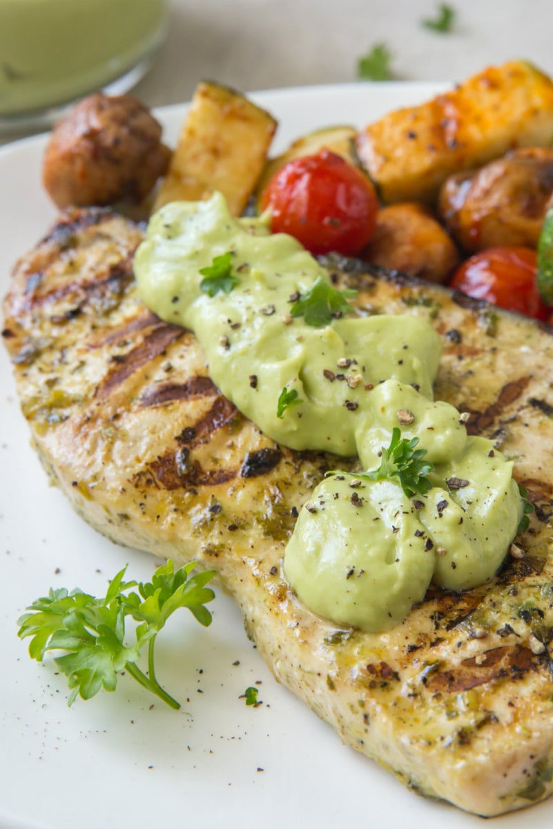grilled swordfish with avocado mayonnaise on a white plate with a side of vegetables
