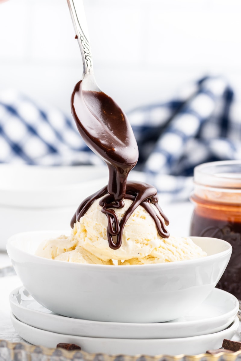 spooning fudge sauce onto ice cream in bowl