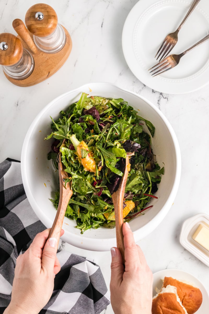 mixed green salad with oranges and dried cranberries being tossed