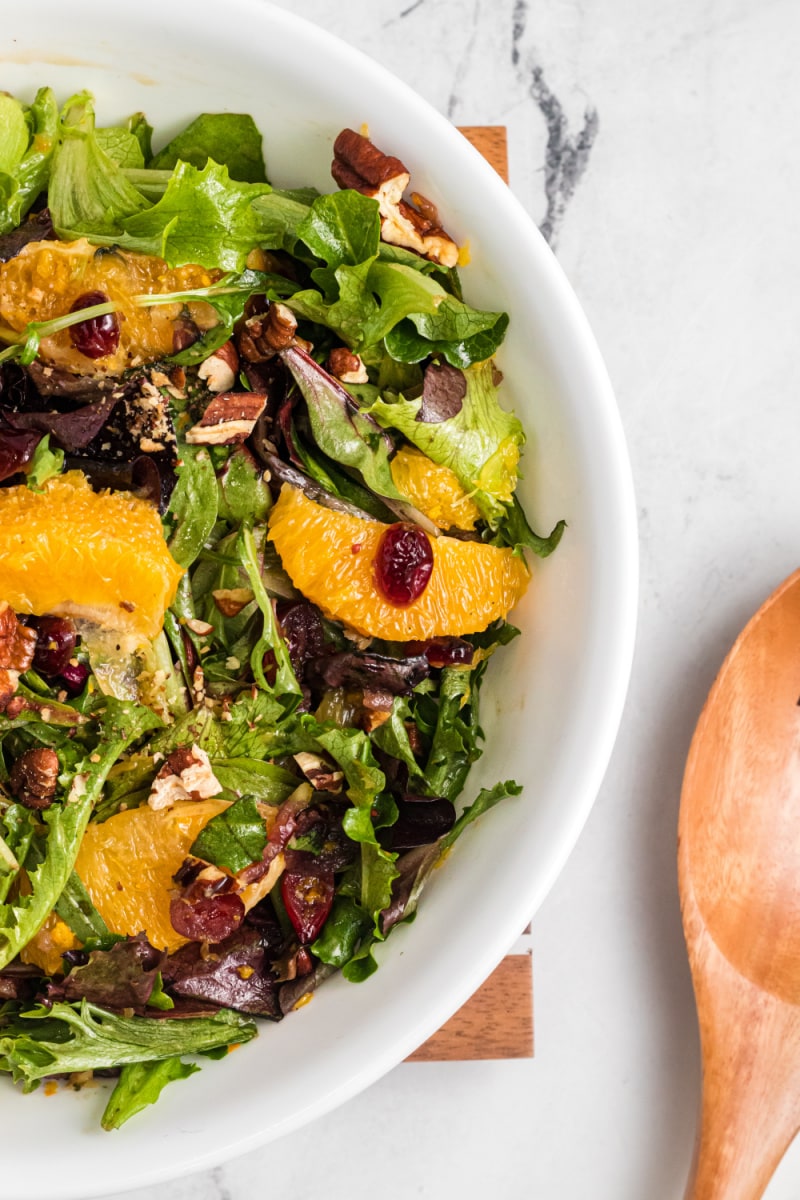 mixed green salad with oranges and dried cranberries in white bowl