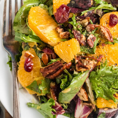 mixed green salad with oranges and dried cranberries on white plate with fork