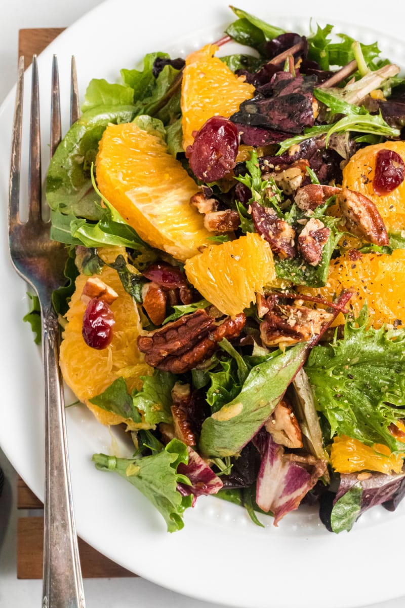 mixed green salad with oranges and dried cranberries on white plate with fork