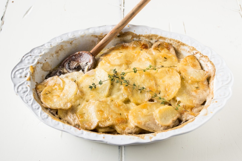 mushroom potato gratin in a dish with a wood spoon