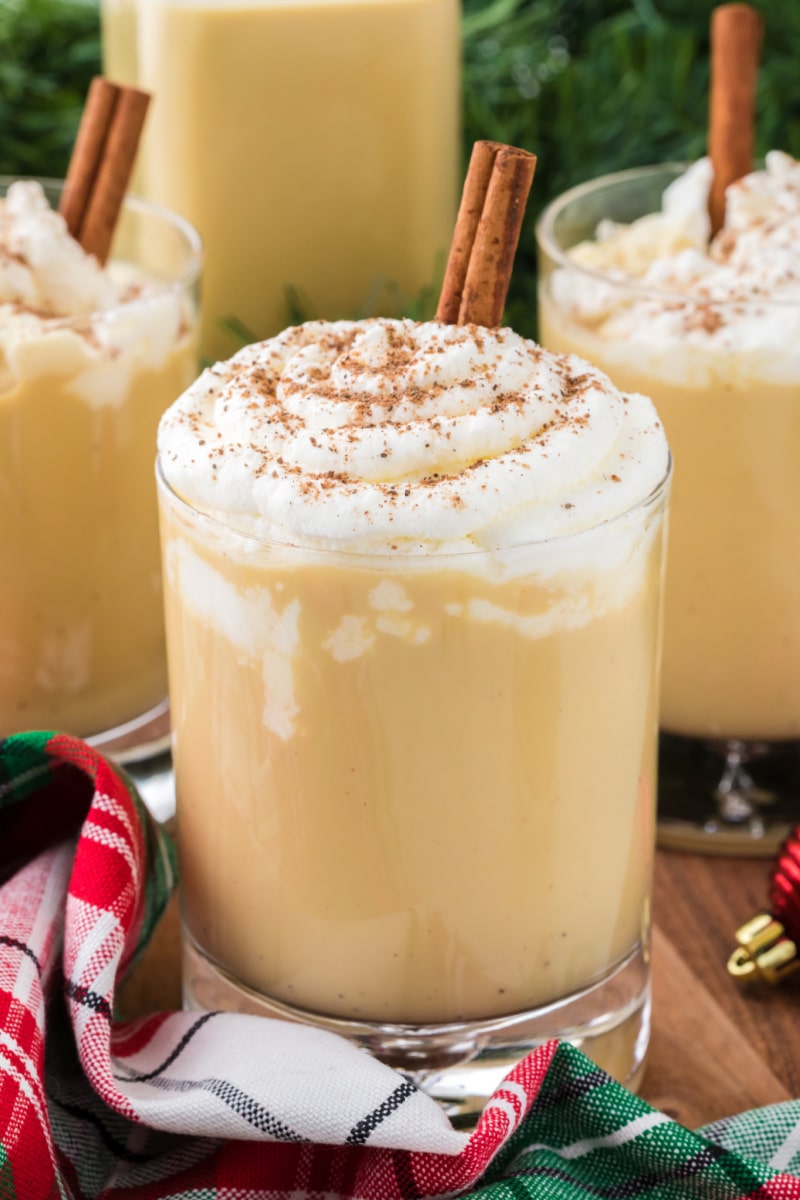 spiked eggnog in a glass mug with whipped cream and cinnamon stick