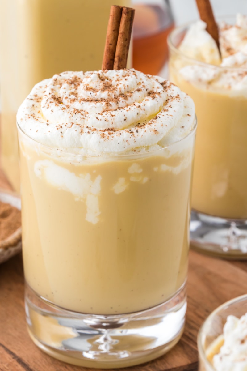 spiked eggnog in a glass with whipped cream and cinnamon stick