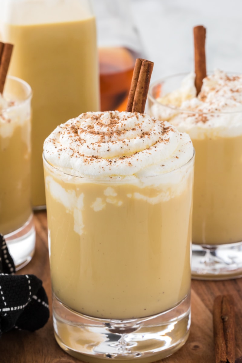 spiked eggnog in glasses with whipped cream and cinnamon sticks