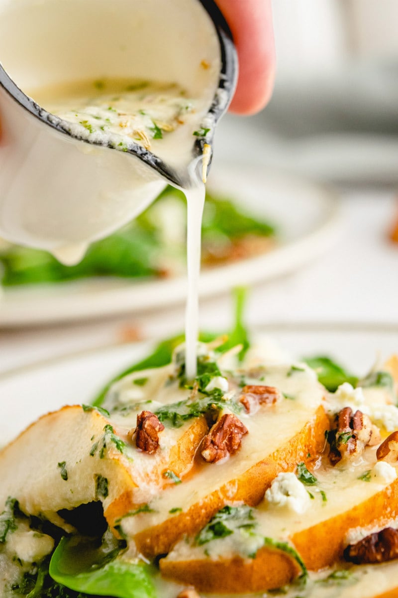 pouring dressing onto spinach and pear salad