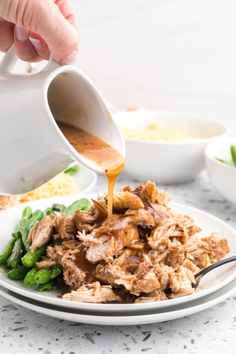 pouring sauce onto shredded pork on plate