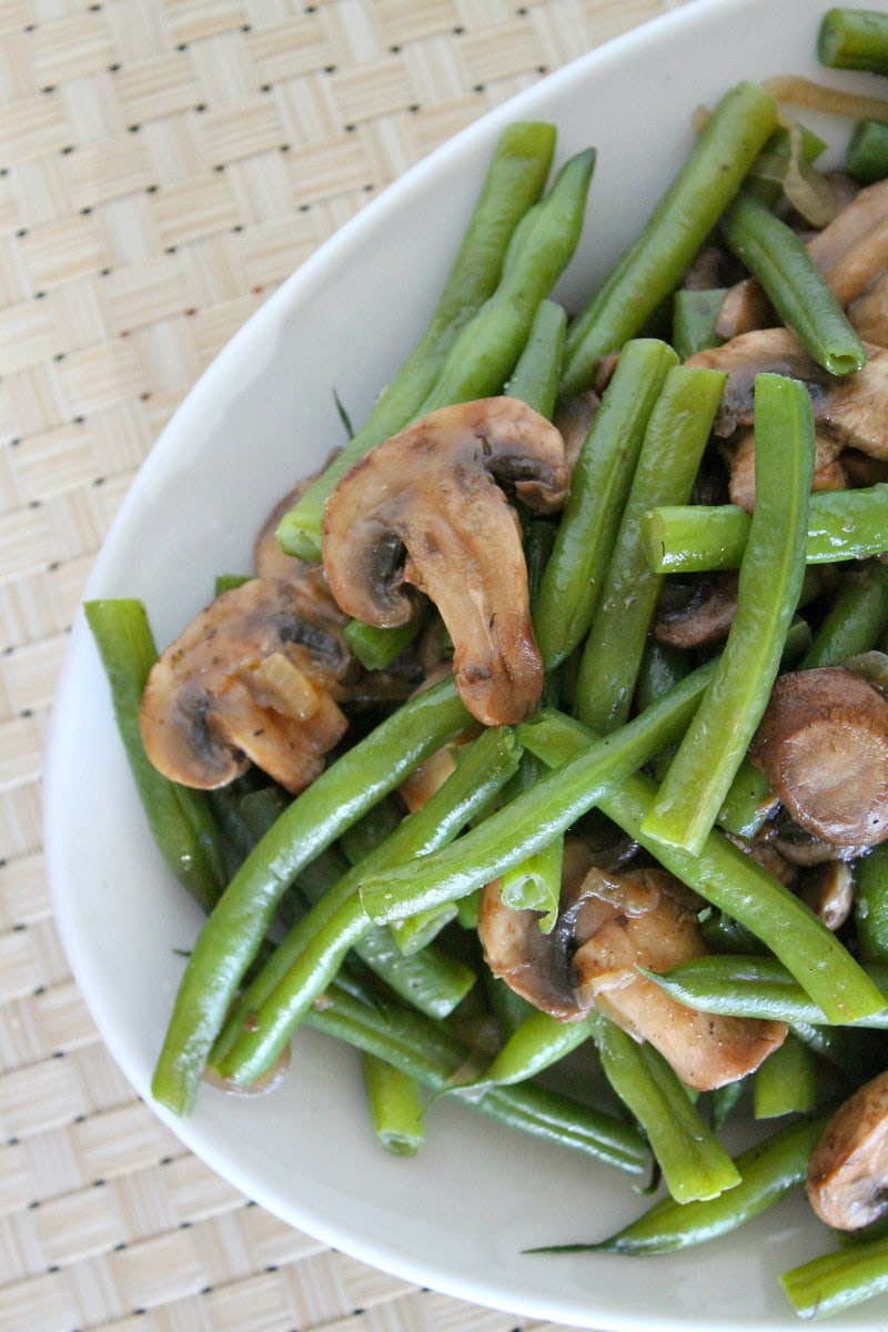 Green Beans with Mushrooms and Shallots on a white platter set on a white woven placemat