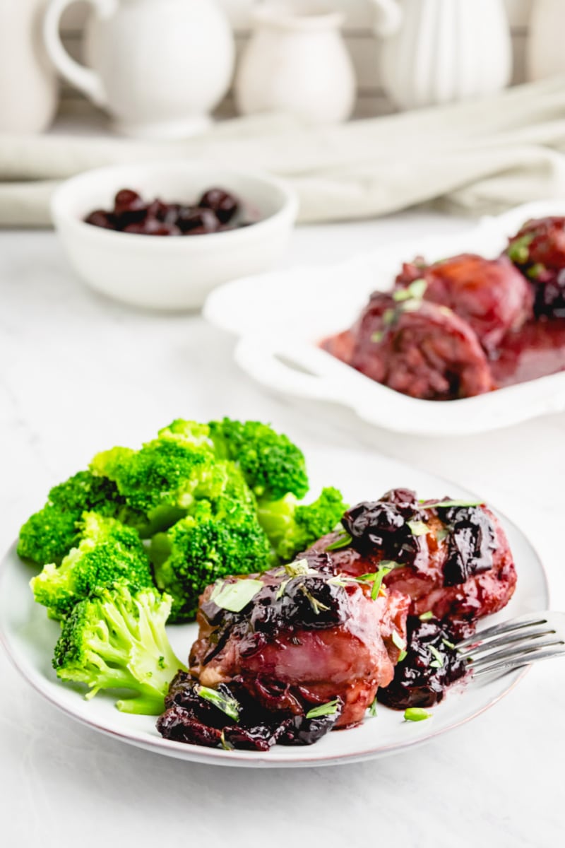 serving of sauteed chicken with cherries on a plate with broccoli