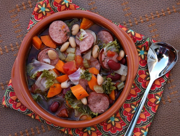 Slow Cooker Tuscan Sausage and Bean Soup in a bowl on a flowered placemat with spoon