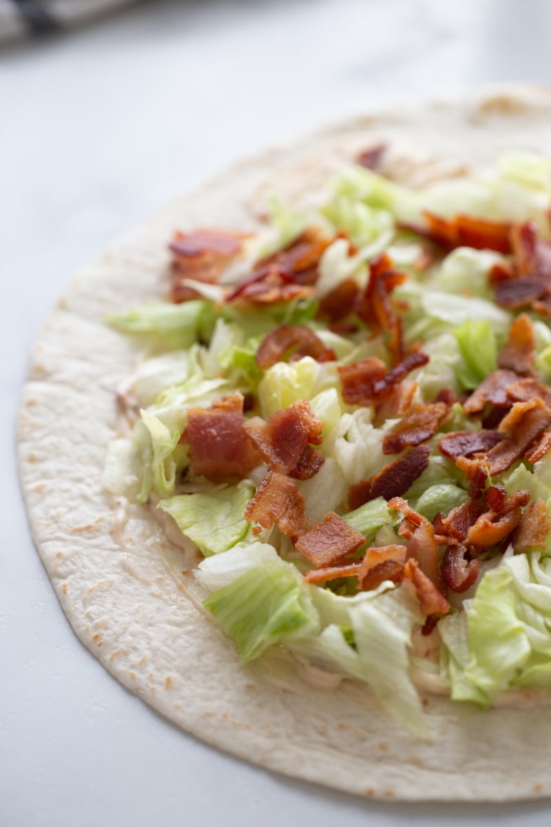 tortilla with sauce, lettuce and bacon spread on it