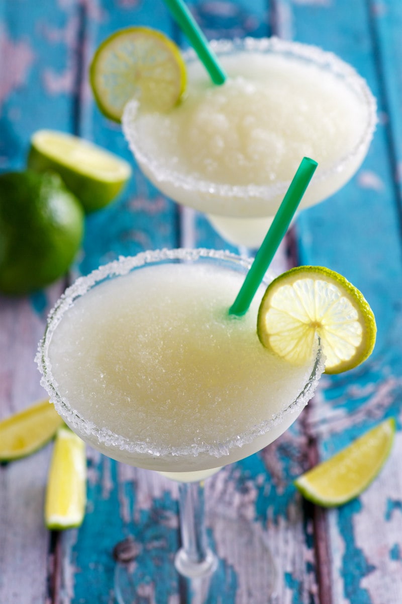 two mock margaritas with lime garnish set on a rustic turquoise board