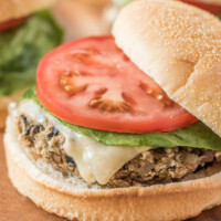 mushroom veggie burger on a wooden board. top of the bun sliding off a bit. tomato and lettuce on the burger too.