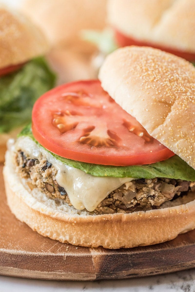 mushroom veggie burger on a wooden board. top of the bun sliding off a bit. tomato and lettuce on the burger too.