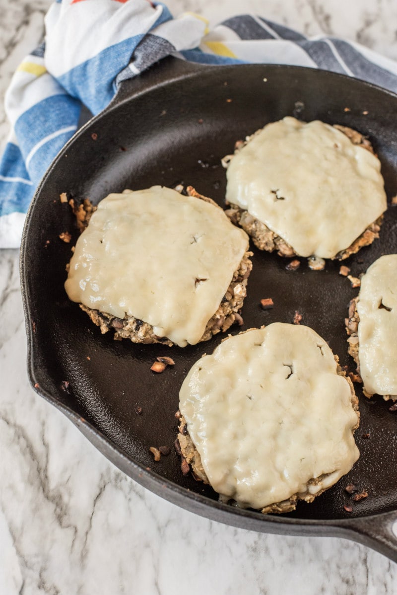 mushroom veggie burgers with cheese on top frying in a skillet