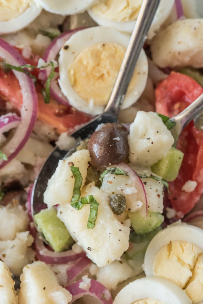close up of spoon of potato salad with olives tomatoes and capers