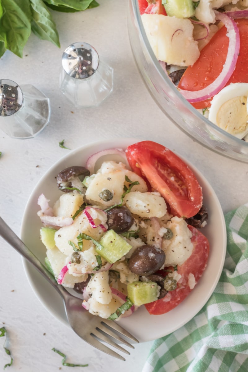 serving on a white plate of potato salad with olives tomatoes and capers