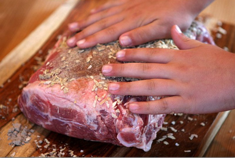 hands rubbing in spices onto pork shoulder