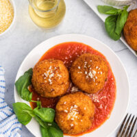 three risotto croquettes on a plate of marinara sauce