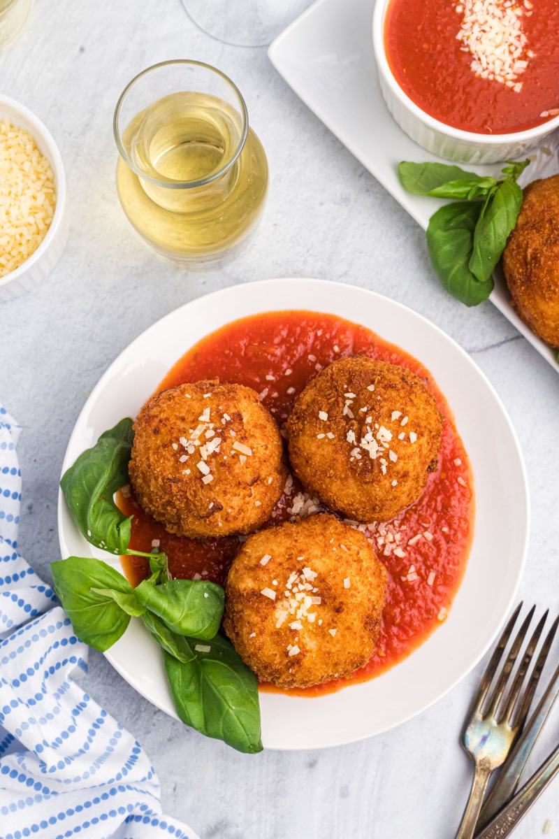 three risotto croquettes on a plate of marinara sauce