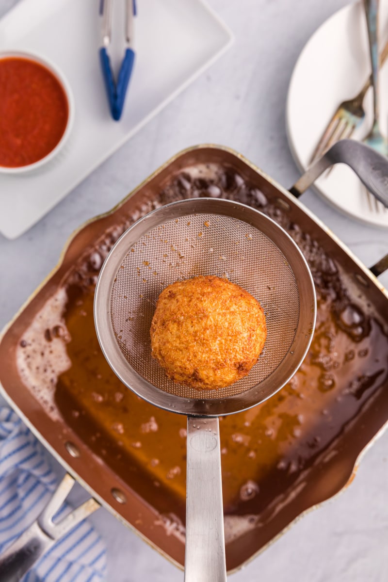 strainer taking risotto croquette out of frying oil