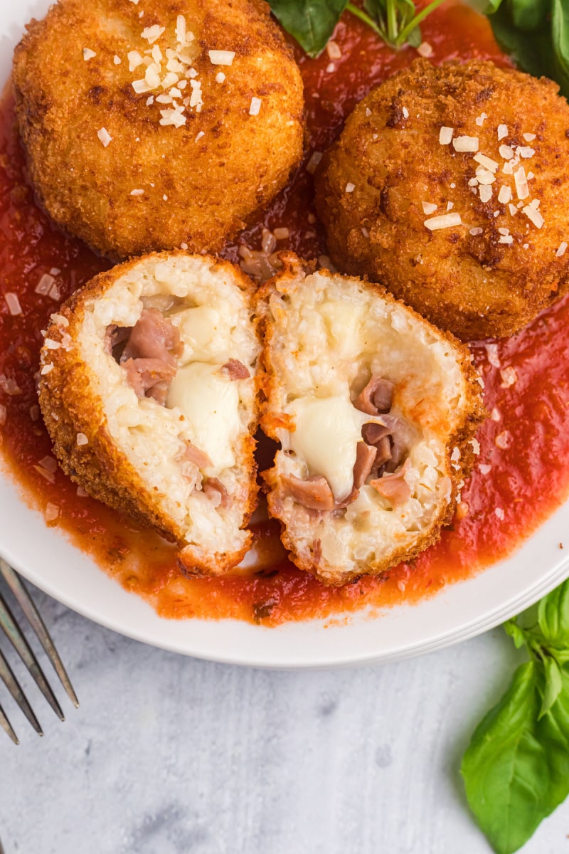 risotto croquettes on plate of marinara sauce one cut in half