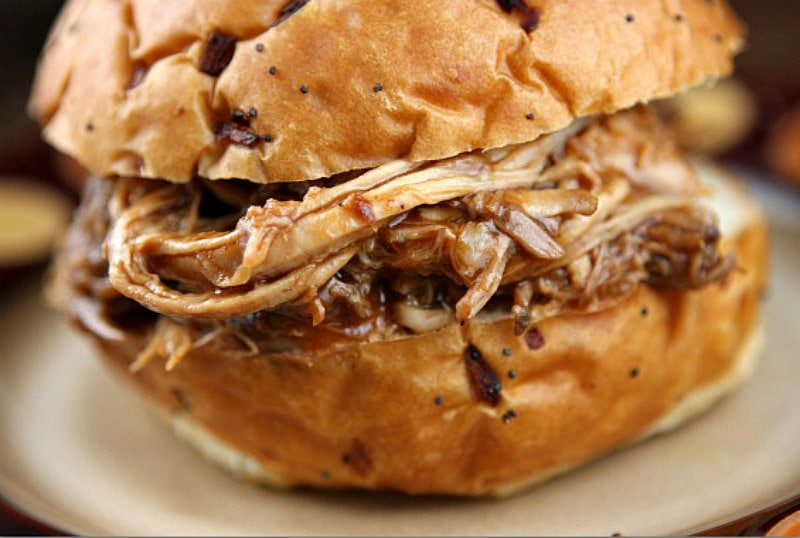 close up showing hamburger bun with pulled pork in the middle, sitting on a white plate