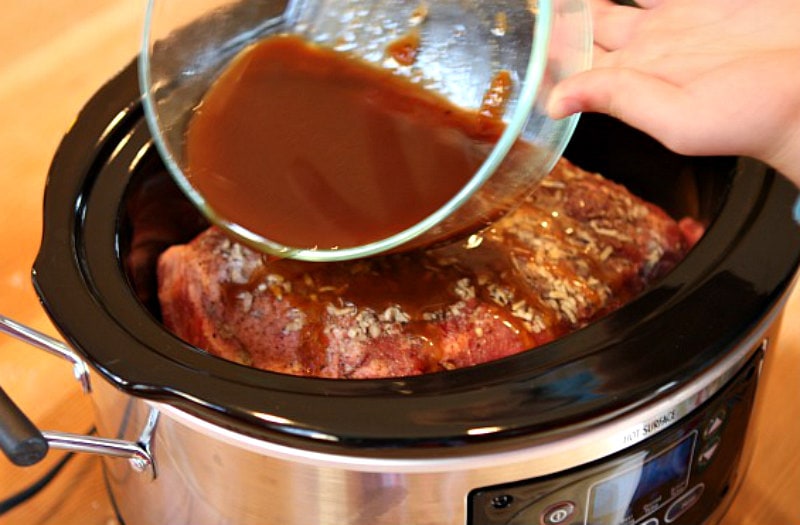 pouring barbecue sauce onto pork roast in a slow cooker