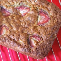 overhead shot of strawberry oatmeal banana bread loaf on a cooling rack over a red cloth napkin