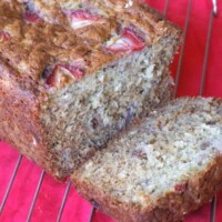 loaf of strawberry oatmeal banana bread sliced open and sitting on a cooling rack on a red cloth napkin