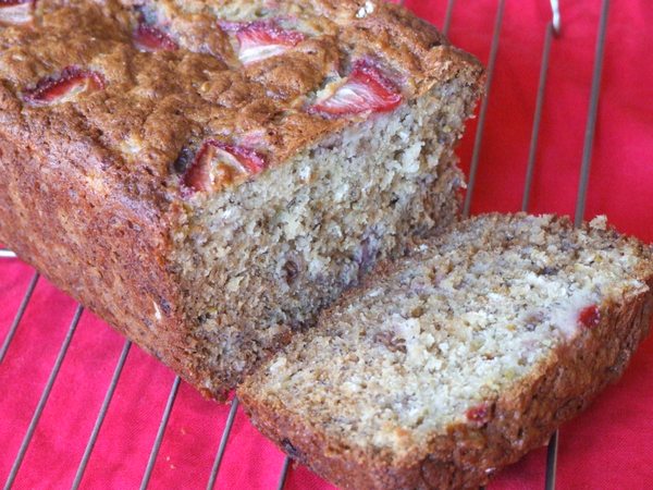 loaf of strawberry oatmeal banana bread sliced open and sitting on a cooling rack on a red cloth napkin