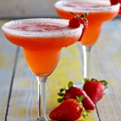 two strawberry margaritas in margarita glasses garnished with strawberries