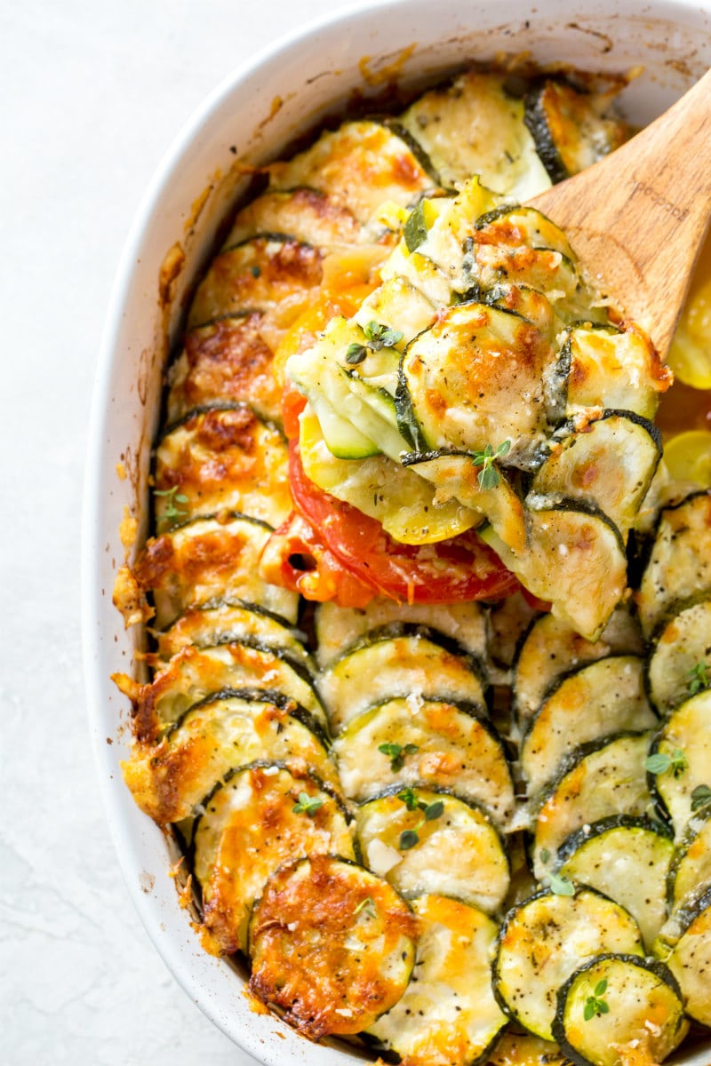 wooden spoon serving summer squash gratin from a white casserole dish