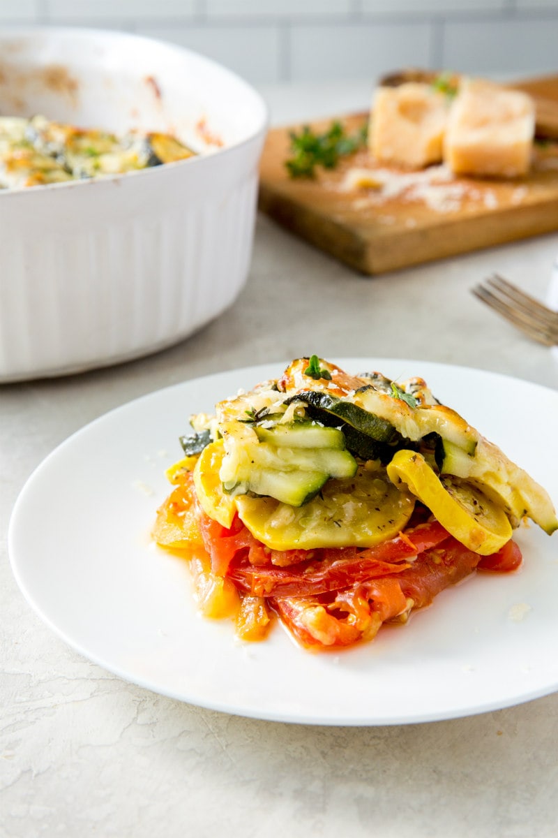 serving of summer squash gratin on a white plate with white casserole dish and cutting board in the background