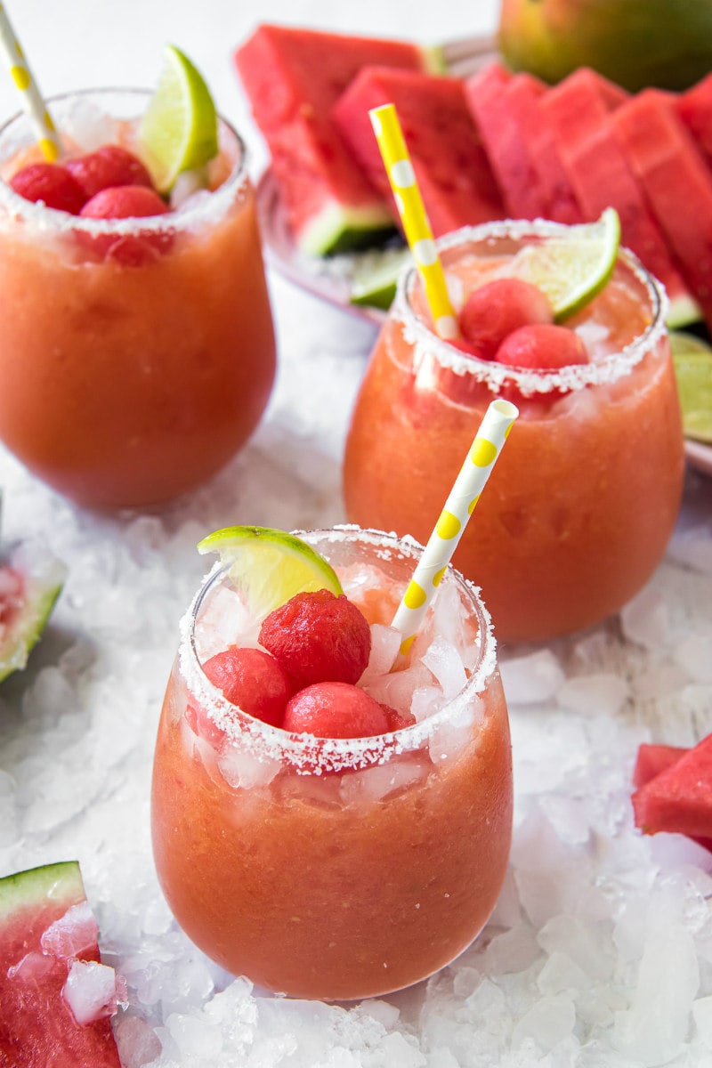 watermelon mango margaritas with yellow straws and watermelon ball garish and lime garnish sitting on a bed of ice