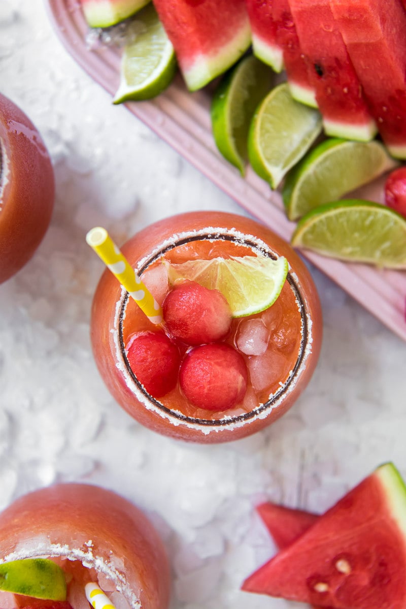 overhead shot of watermelon mango margarita with yellow straw with watermelon balls and lime wedges garnished on the side